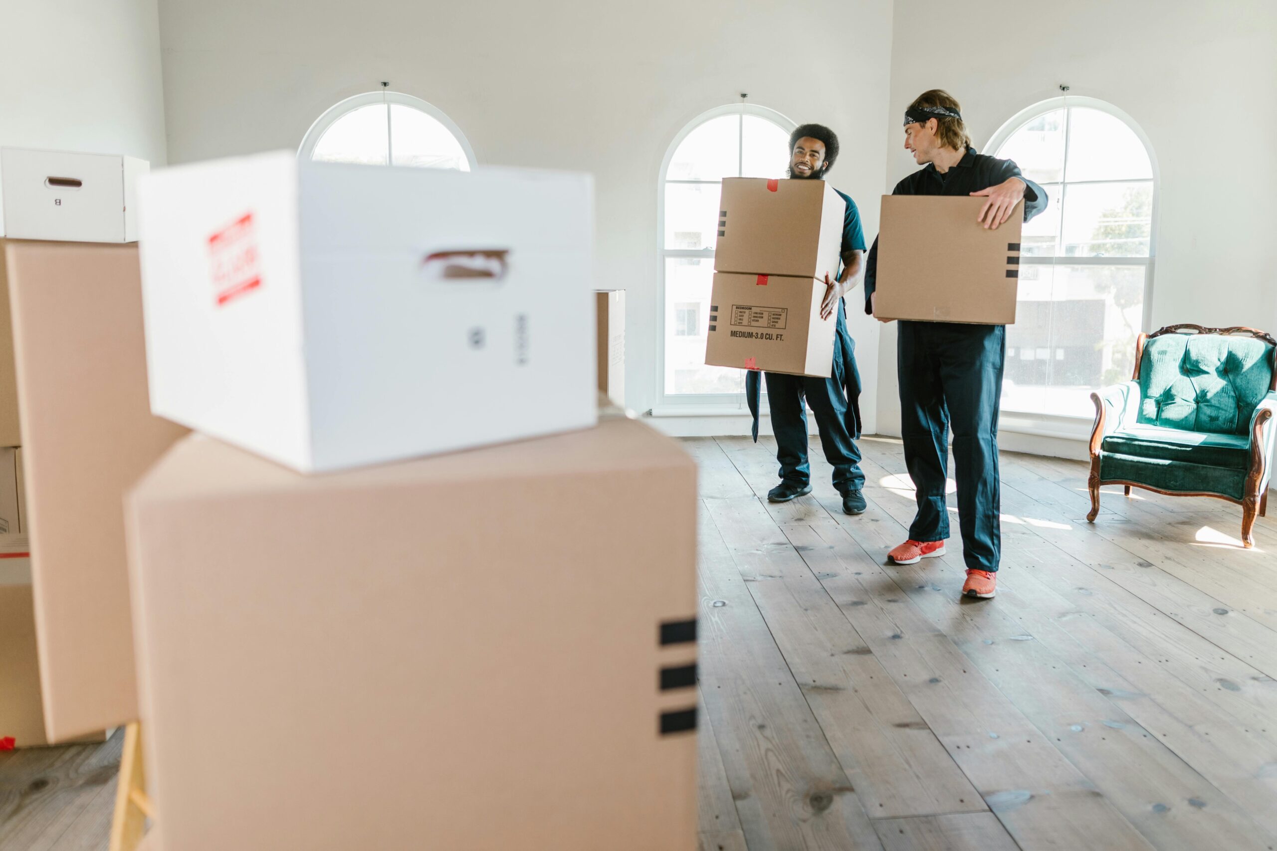 Two movers in uniform carrying boxes in a bright, new home setting.